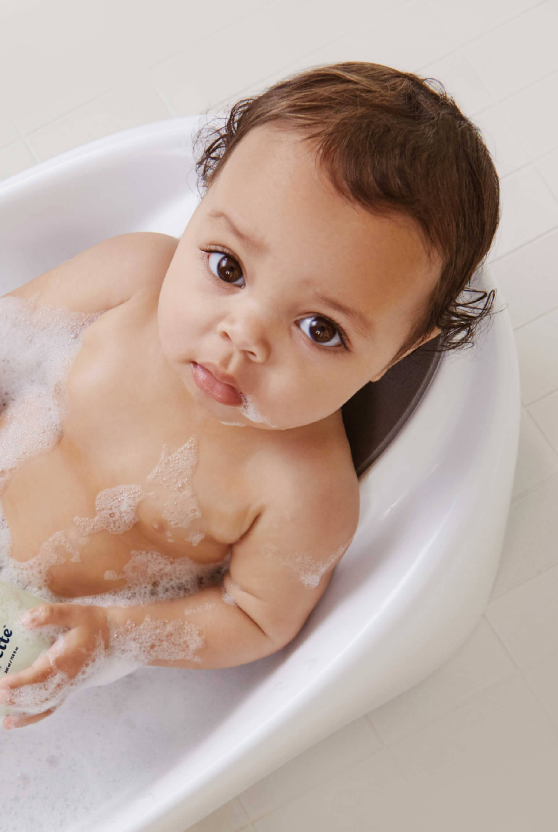 Baby in tub holding Baby Shampoo + Wash